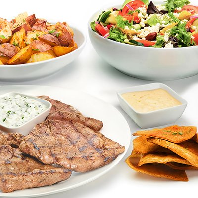Chargrilled Lamb Family Feast with roasted potatoes, a Greek salad with tomatoes and cheese, and baked pita chips