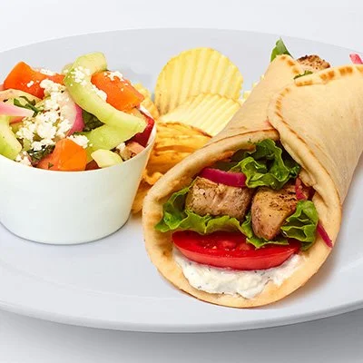 a photo of a grilled chicken gyro with a side of cucumber tomato salad and potato chips