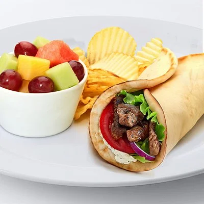 An image of the grilled lamb gyro on a white plate with a side of fresh fruit and potato chips