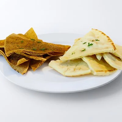 a photo of a small white plate with triangular pieces of golden-brown baked pita chips and cut soft pita bread