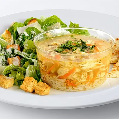 a photo of a plate with a bowl of greek lemon chicken soup and a side of caesar salad