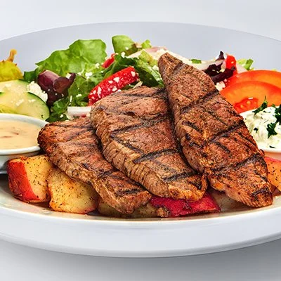 an image of the chargrilled lamb feast, showing medallions of grilled lamb atop a bed of roasted red potatoes with a side greek salad