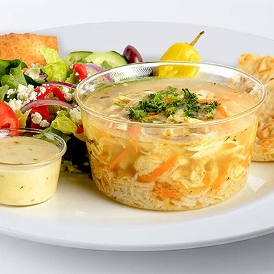 A photo of a plate with a cup of greek lemon chicken soup and a side of greek salad
