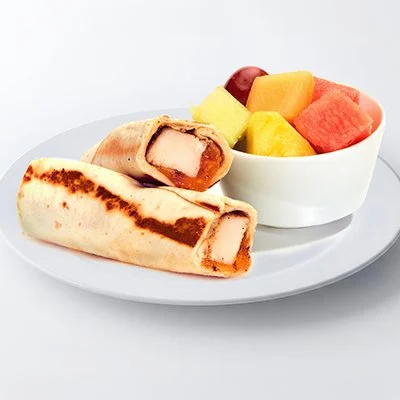 a photo of the "sneaky taziki" kid's menu item with a griddled tortilla that's been rolled around grilled chicken and melting cheddar cheese on a white plate with a side dish of fresh cut fruit