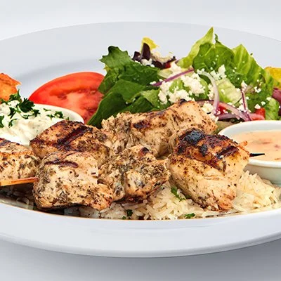 the grilled chicken kebob feast showing two grilled chicken kebobs atop oa bed of rice with a small greek side salad