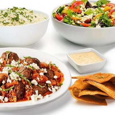 a photo of the turkish meatball family feast, showing a plate full of meatballs covered in rustic tomato sauce with crumbled feta and fresh basil, accompanied by basmati rice and greek salad
