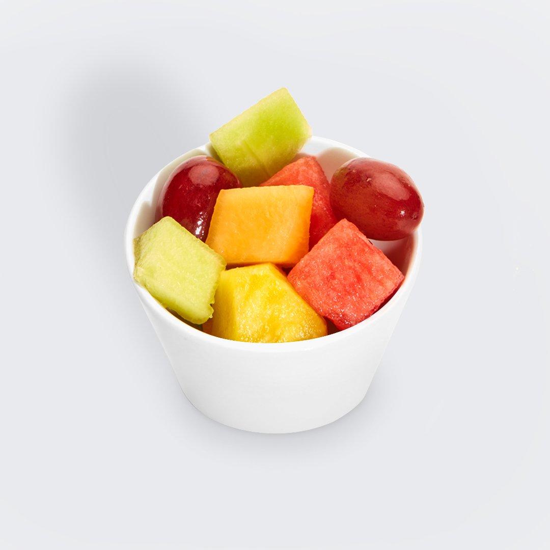 a photo of a small white bowl with pieces of honeydew, pineapple, cantalope, watermelon, and red grapes