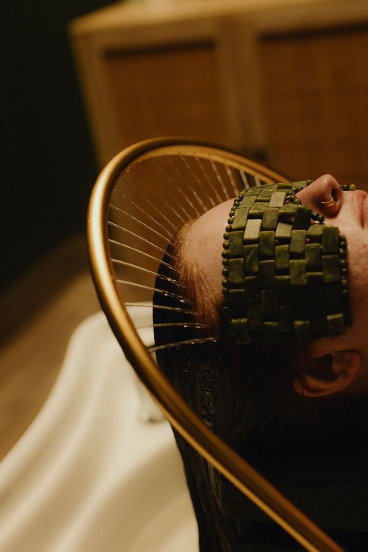 A person lying on a treatment table with a metal headband and a wire mesh pillow supporting their head during a scalp acupuncture or treatment session.
