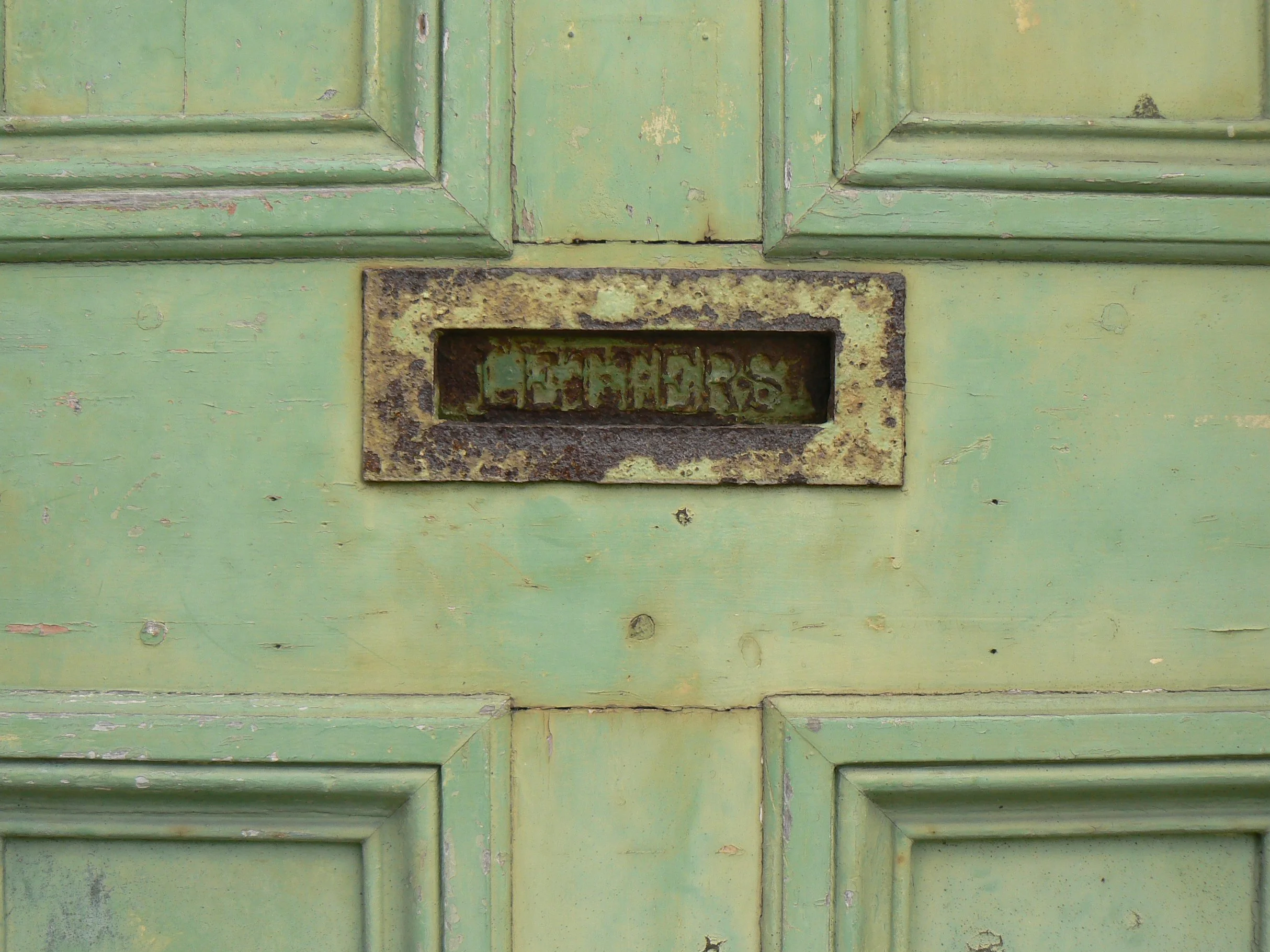 Heritage joinery - a traditionally made Georgian 4 panel entrance door, coated in faded green lead based paint with a rusty letterbox that says 'LETTERS'.