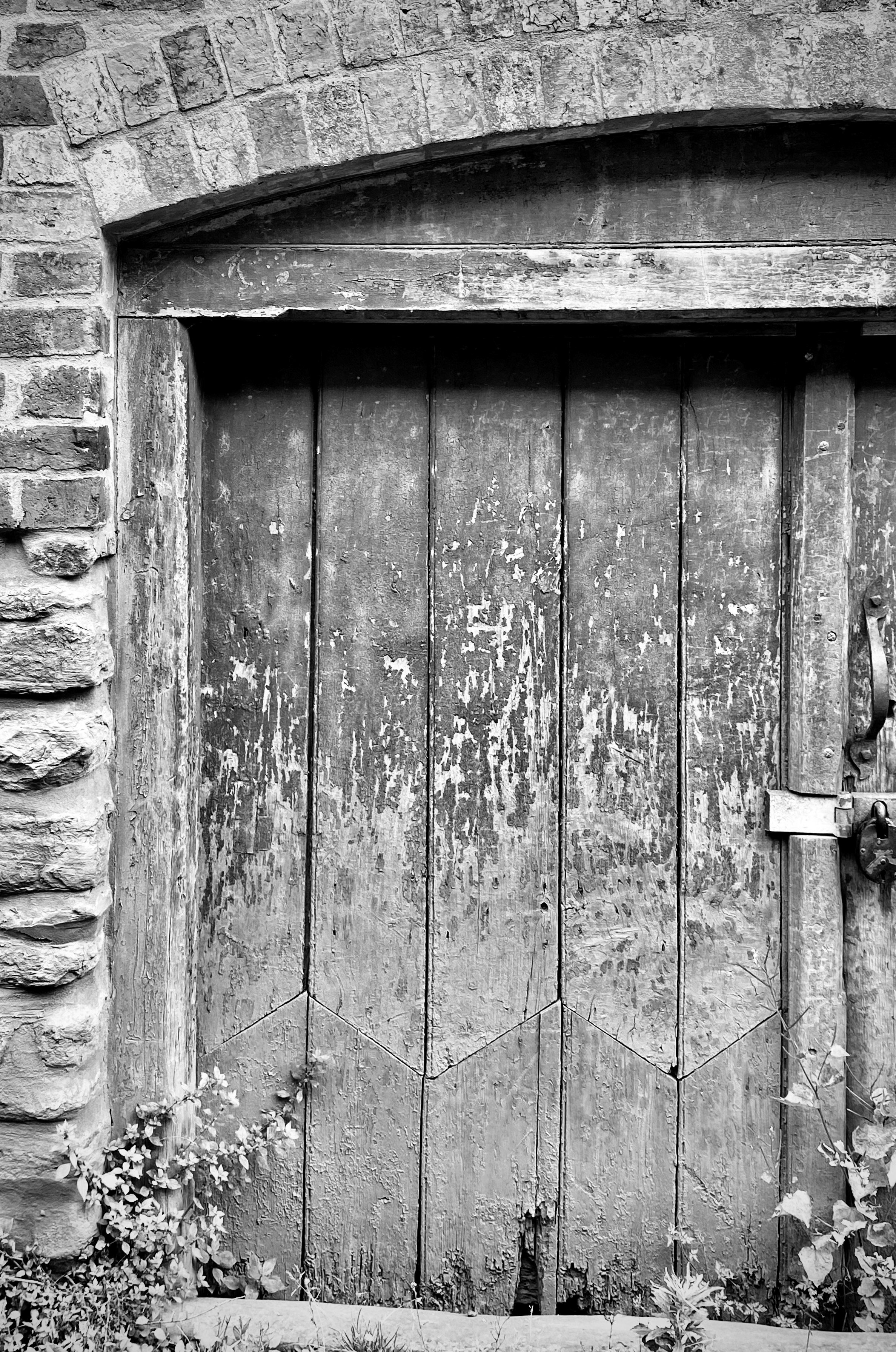 Specialist assessment of historic joinery - black and white photo of a weathered wooden door with a distinctive pattern of previous repair to the lower section.