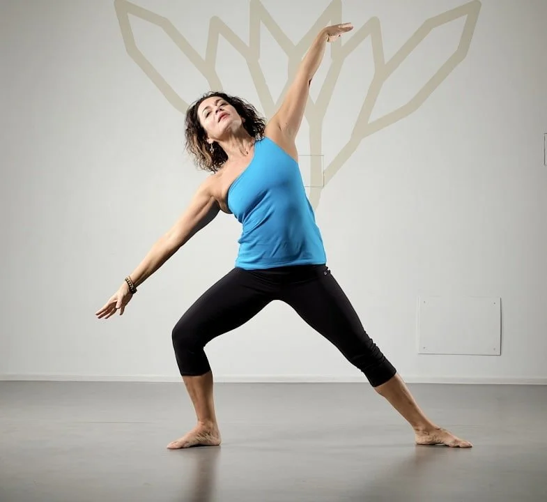 Una donna che fa yoga in una stanza con sfondo di un disegno stilizzato di un albero.