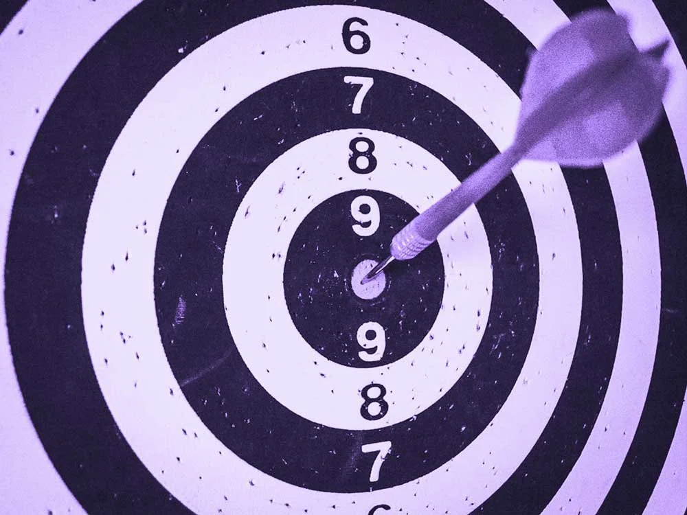 A purple dart hits the bullseye on a black and white dartboard.