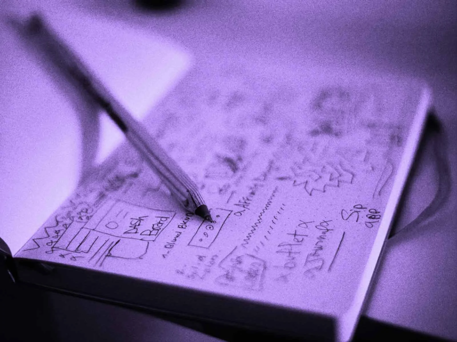 Close-up of a handwritten notes and sketches on a piece of paper with a pen resting on it, under purple light.