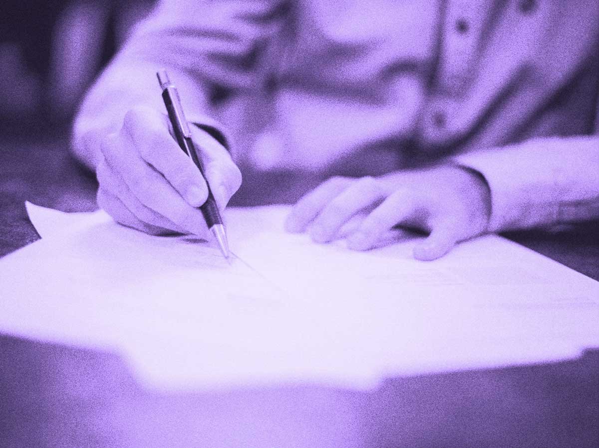 A person's hand writes with a pen on a piece of paper.