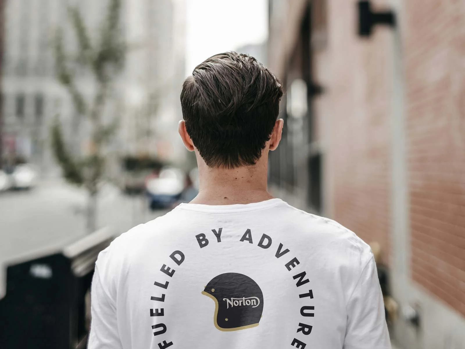Man wearing a white t-shirt with a Norton helmet graphic and "Fuelled by Adventure" text.