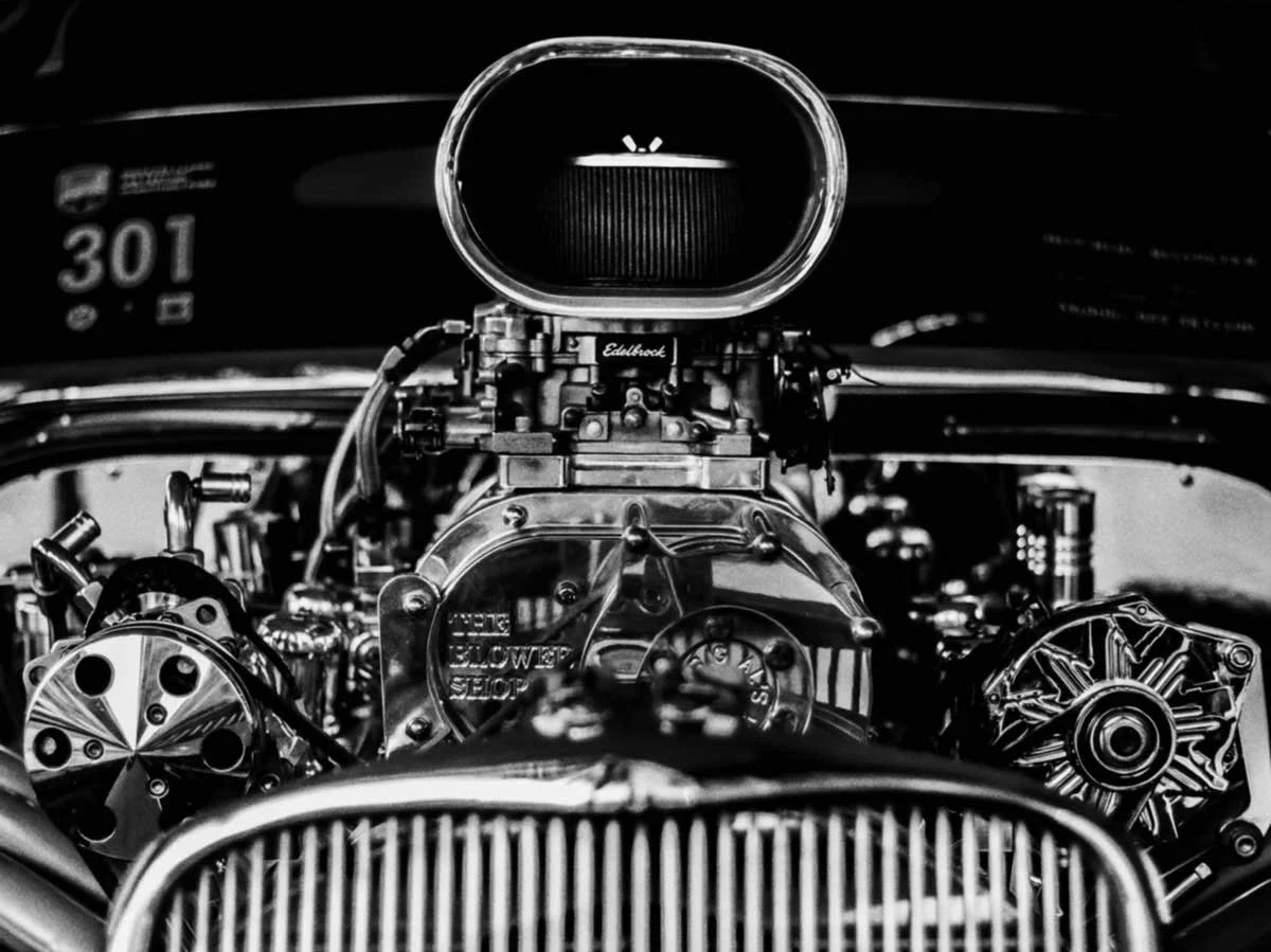 Close-up view of a vintage car engine in black and white, showcasing various mechanical components and parts.