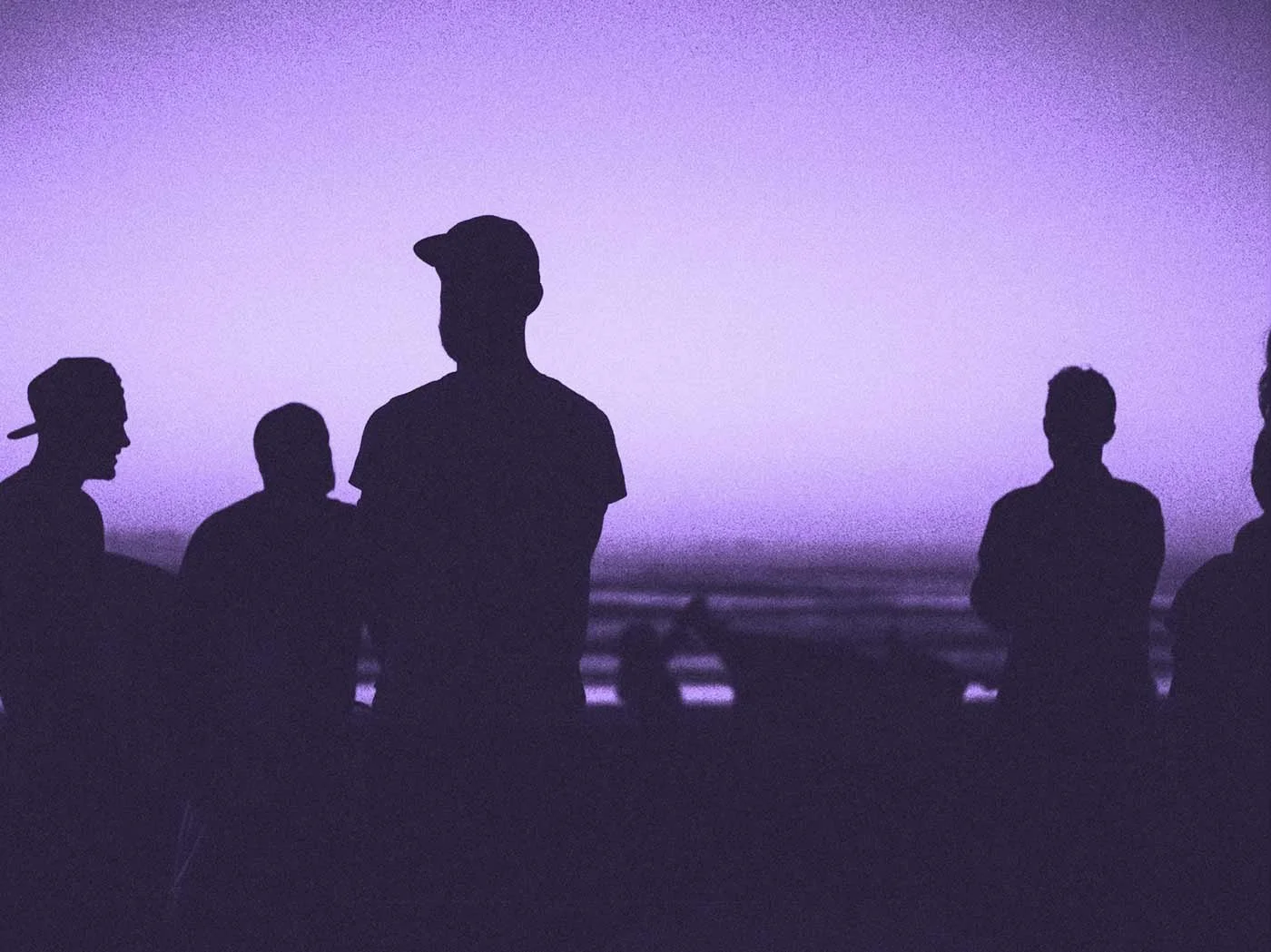 Silhouettes of a group of people standing against a purple sky.