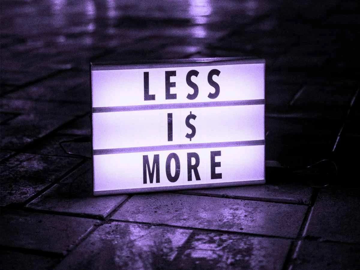 A light-up sign displays "LESS IS MORE" in black lettering on a purple background.