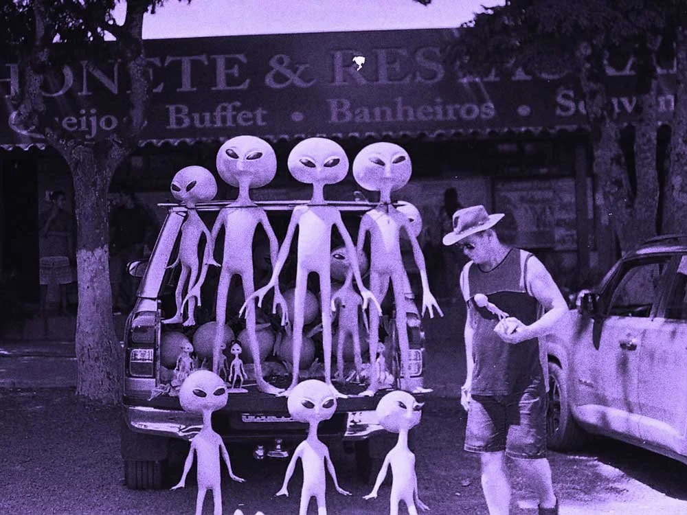 A man in a hat stands next to a pickup truck filled with alien figures.