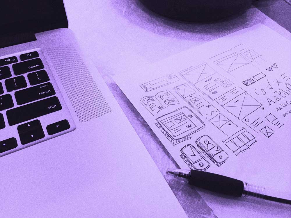 Laptop with wireframe sketches and pen on a desk.