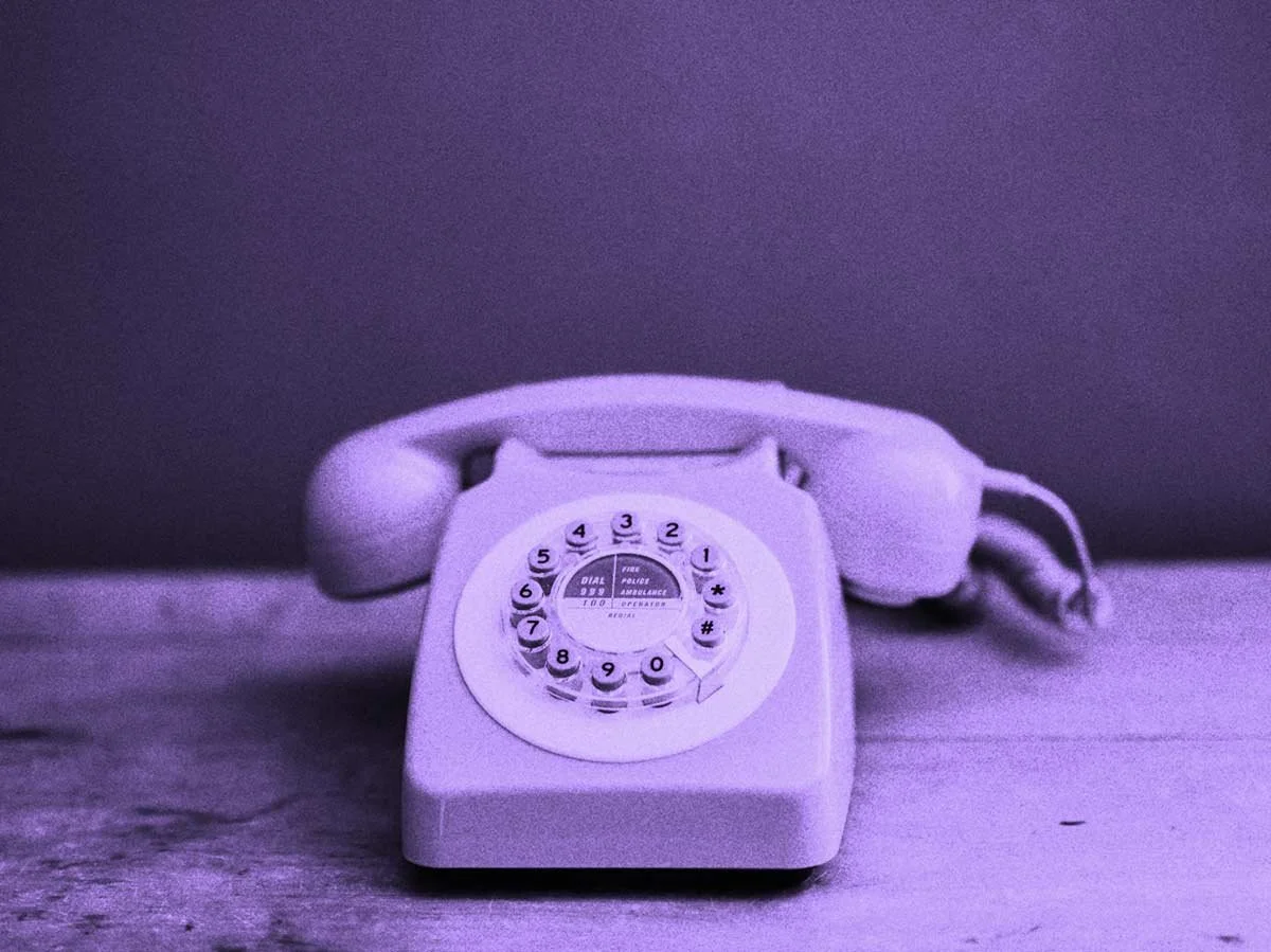 A vintage rotary phone with a dial is shown in purple tones.