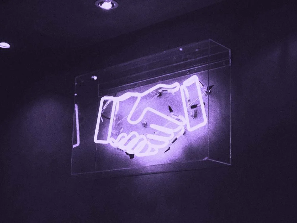 A purple neon sign displays a handshake inside a clear box.