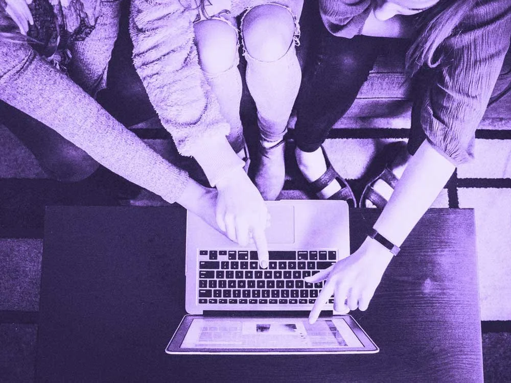 Several people point at a laptop screen.