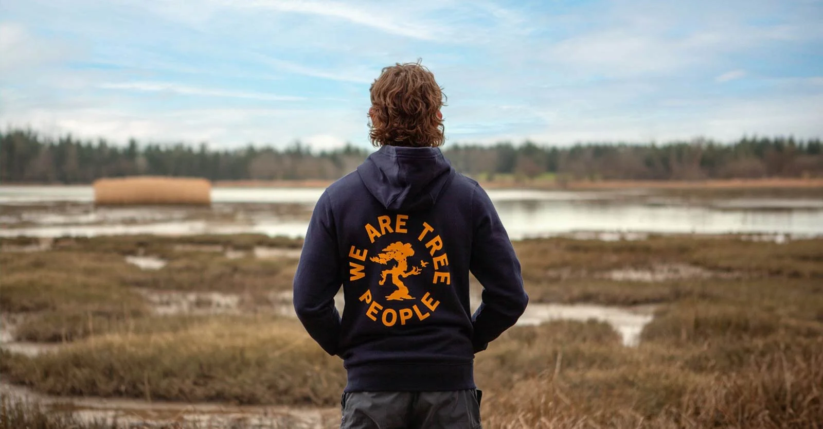 Person in a navy hoodie with "WE ARE TREE PEOPLE" graphic standing in a marsh.