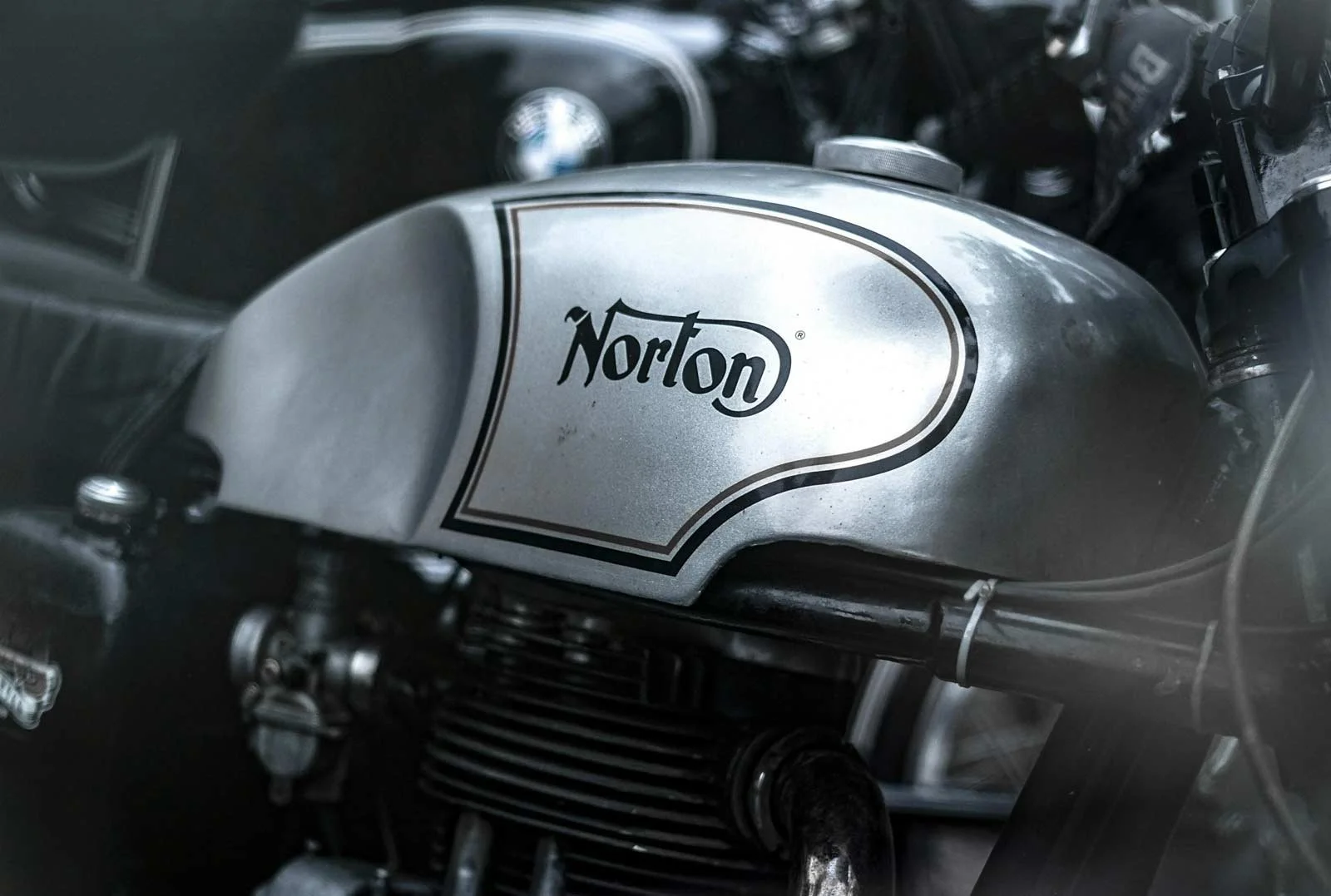 A close-up of a silver Norton motorcycle fuel tank with the brand name clearly visible.