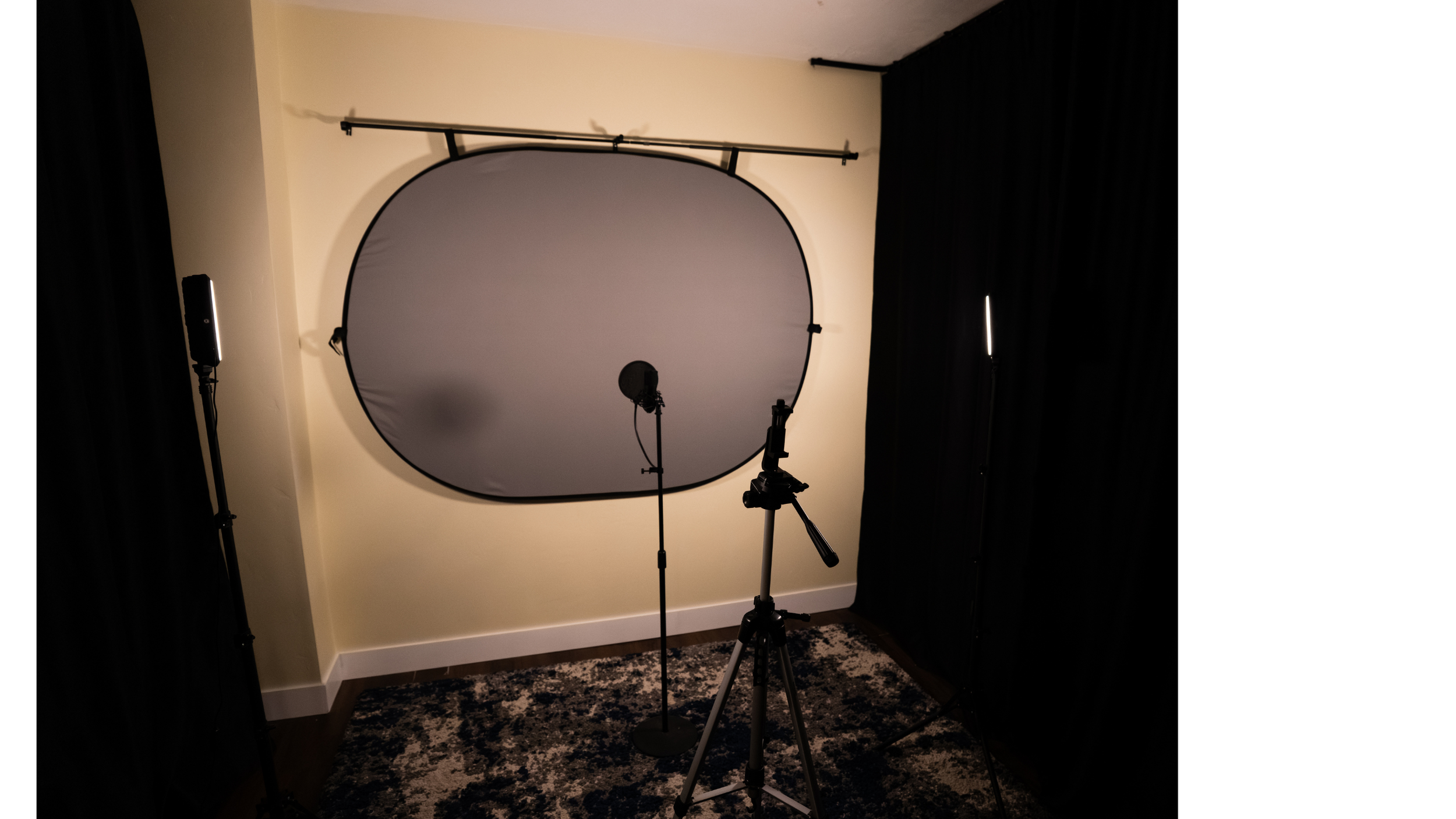 Photography studio setup with a large collapsible backdrop, professional lighting, a microphone on a stand, and a tripod inside a room with black curtains on both sides.