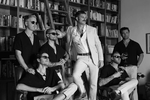 Groomsmen posing confidently in a wood-panelled library with floor-to-ceiling bookshelves and a ladder