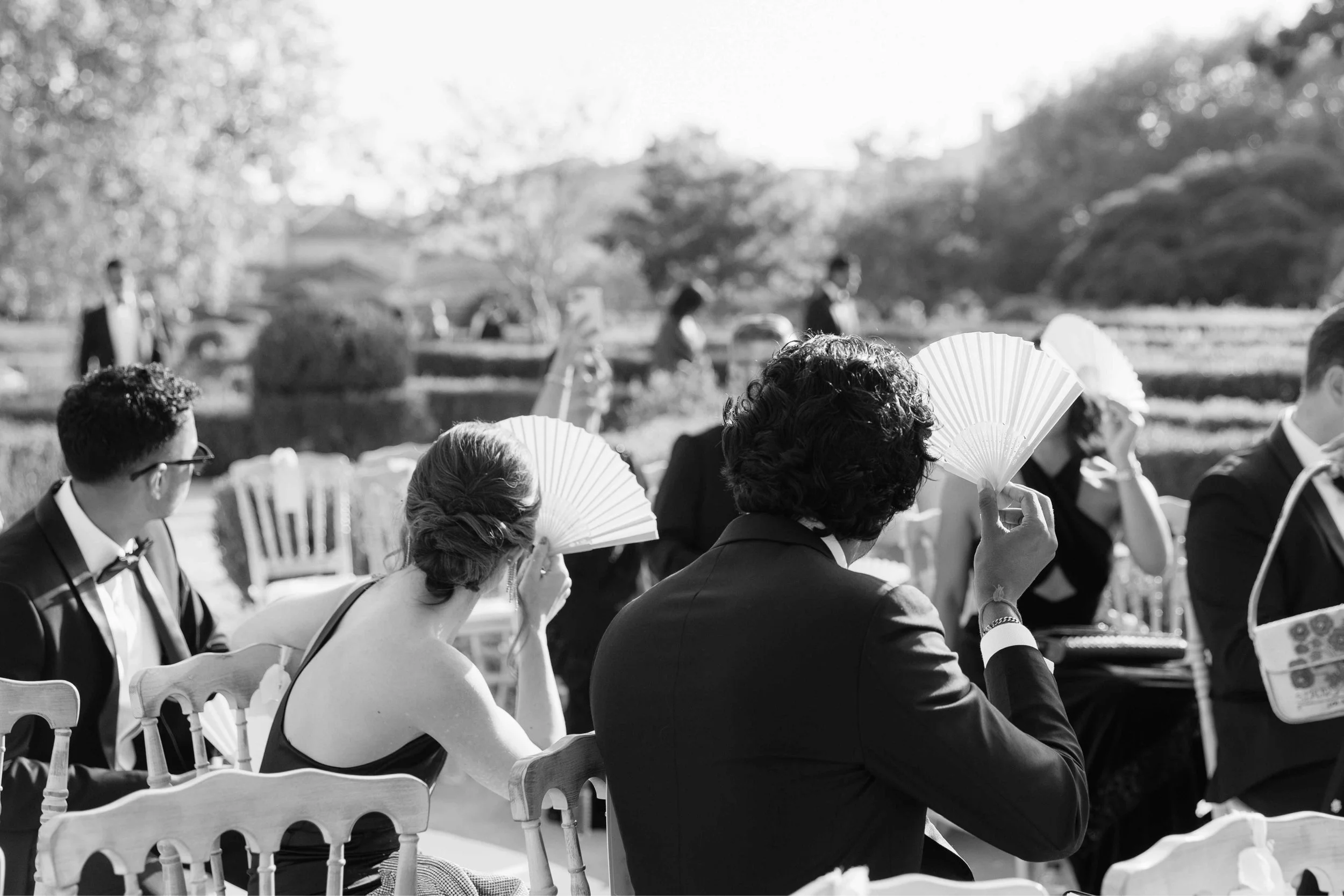 Guests holding up fans go shade faces from the sun at a luxury wedding in Marbella