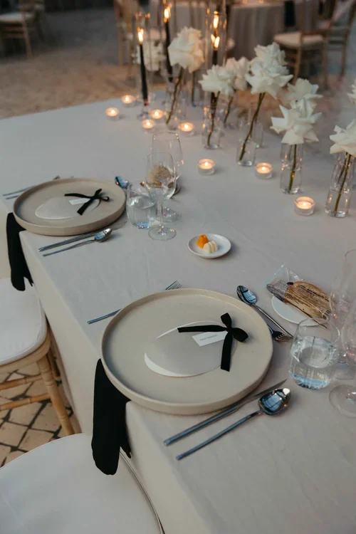 Elegant wedding reception place setting with ceramic plates, black bow napkins and white floral centrepiece with tea lights