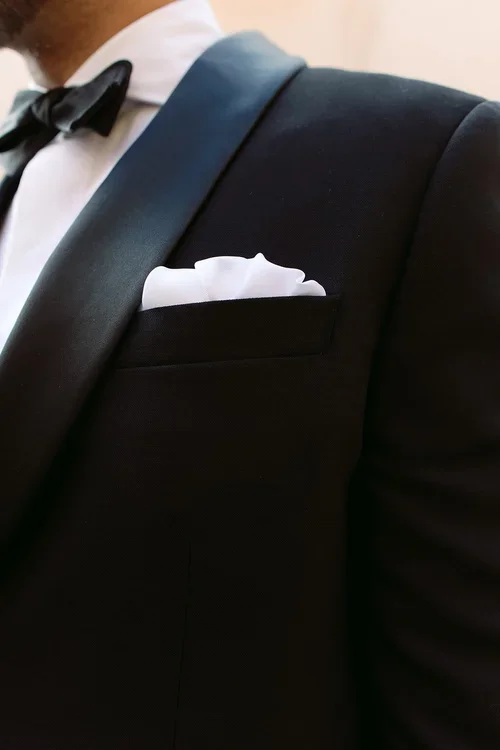 Close-up of groom's black tuxedo with silk bow tie and white pocket square