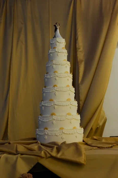 Tall eight-tier white fondant wedding cake with decorative ruffles and bride and groom topper, grand wedding cake