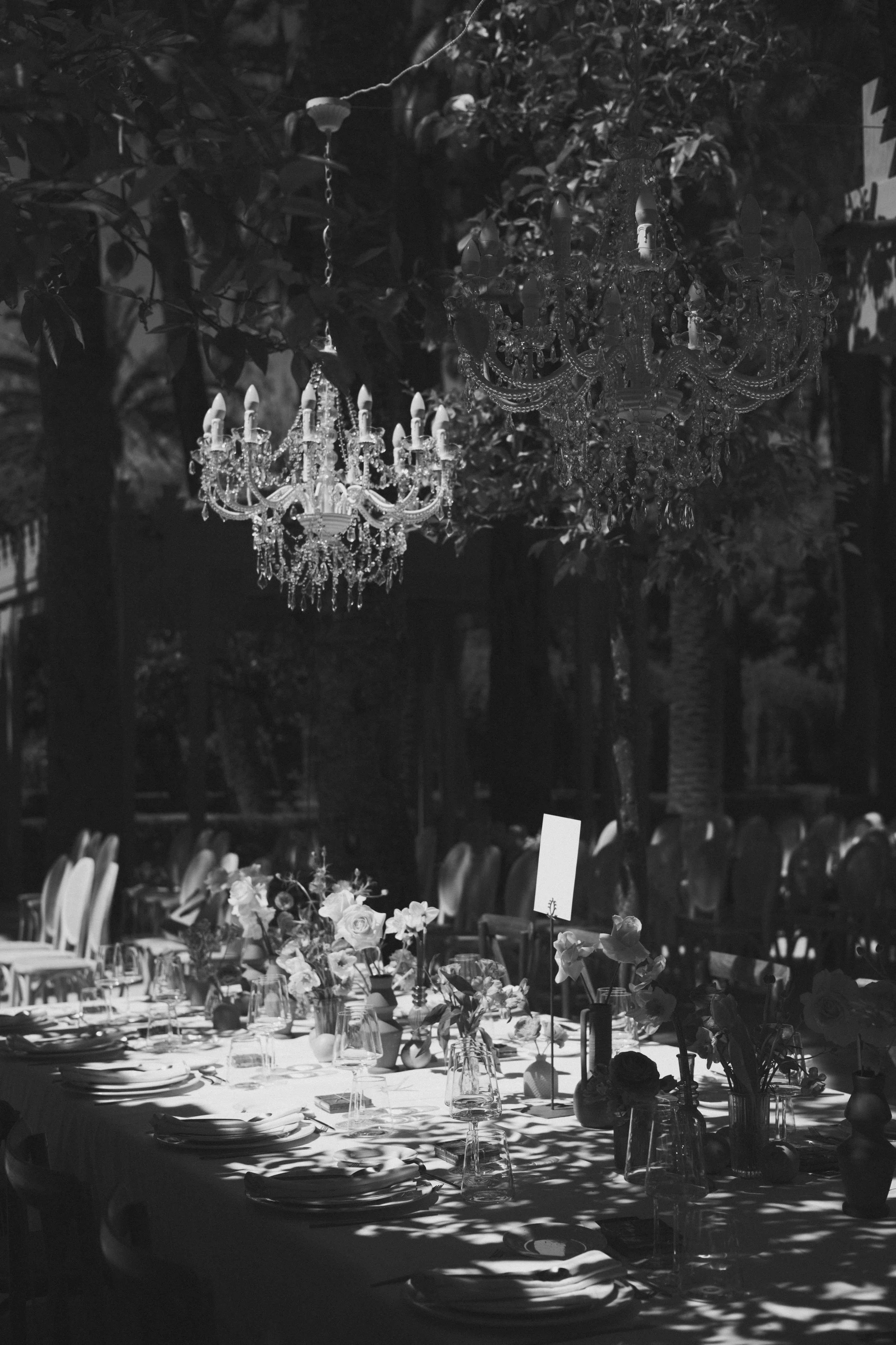 Glamorous outdoor evening wedding reception with crystal chandeliers hanging between trees and a floral long table