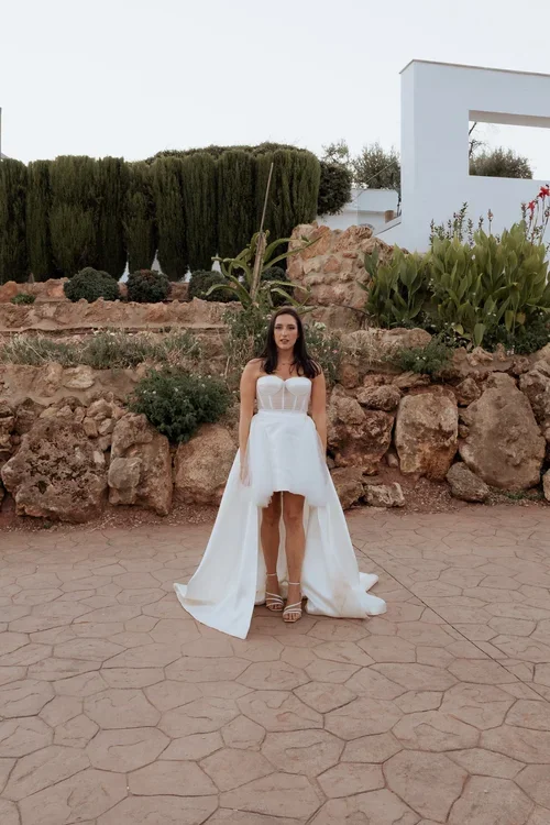 Bride in strapless corset bodice high-low wedding dress standing in front of a rocky Andalusian garden at an outdoor wedding venue in Malaga