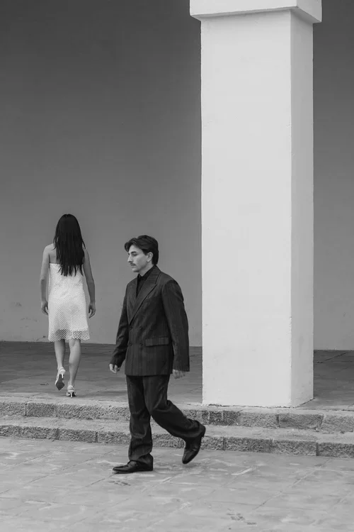 Bride in short white mesh dress walking away and groom in pinstripe suit walking in opposite directions beside a large white stone pillar at a Barcelona wedding venue