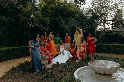 Bride in white dress surrounded by bridesmaids in vibrant colourful dresses around a stone water fountain in a Malaga garden