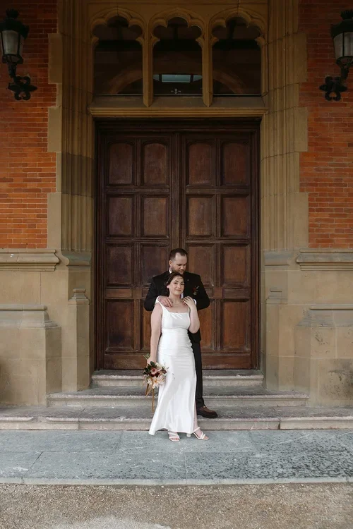 Bride and groom standing in front of a grand ornate wooden doorway with Gothic carved stonework