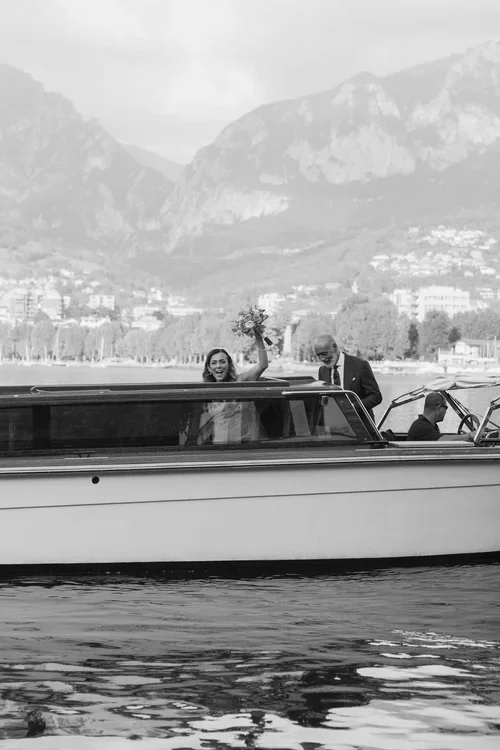 Bride arriving by classic Riva motorboat on Lake Como with mountains in the background