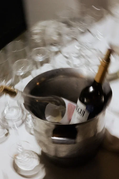 Artistic motion-blur photograph of a wine bottle in a silver ice bucket surrounded by crystal wine glasses on a white tablecloth at a Spanish wedding reception