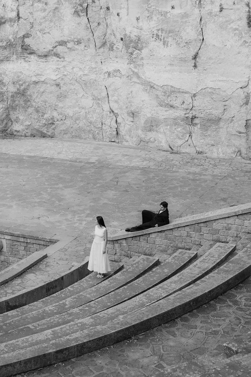 Bride and groom at the ancient Roman amphitheatre in Malaga, bride standing at the base and groom reclining on the stone steps