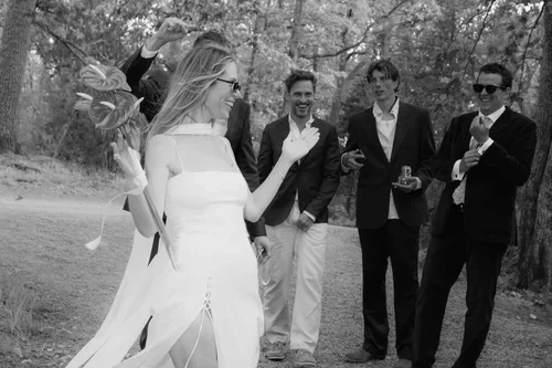 Bride in white halterneck dress and sunglasses laughing and dancing with male wedding guests in dark suits among pine trees at a Malaga wedding reception