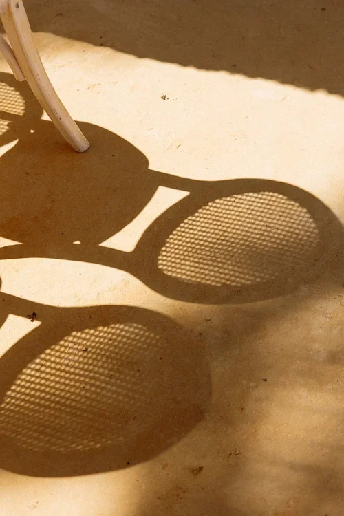 Artistic shadow of woven rattan wedding chairs cast on a golden sandy floor in the Malaga sunshine