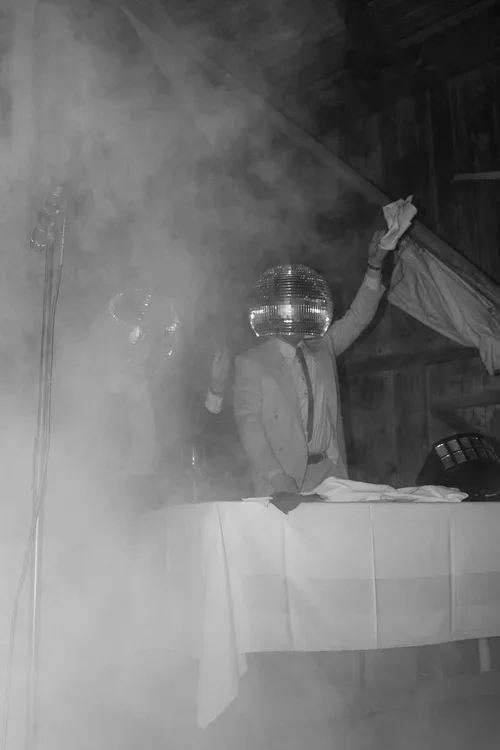  DJ wearing a mirror disco ball face mask performing on stage surrounded by smoke at a wedding evening reception