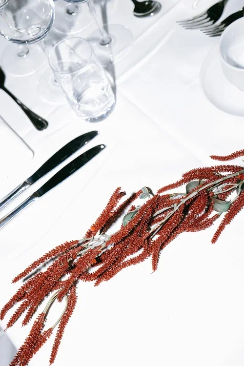 Wedding table set up with glassware black cutlery next to red dried amaranth flowers
