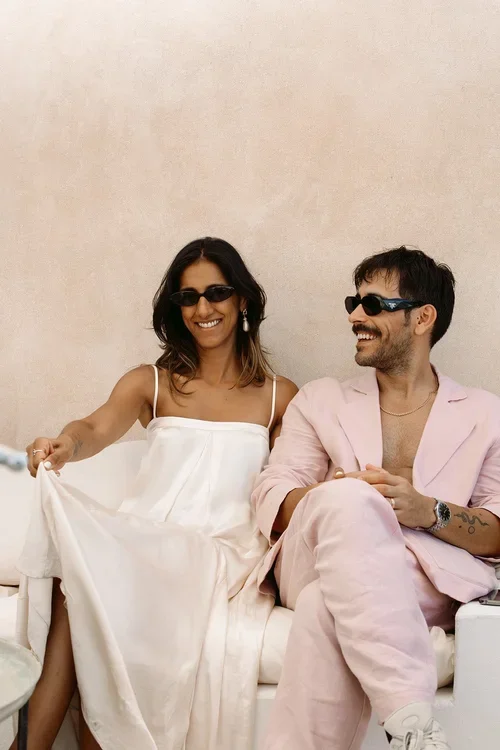 Relaxed candid portrait of bride in white slip dress and groom in pink linen suit laughing together in Marbella