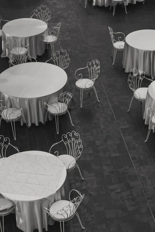 Aerial overhead black and white view of round Malaga wedding reception tables with white satin cloths and ornate wrought iron peacock chairs on a dark tiled floor