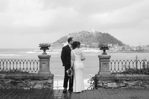 Bride and groom kissing on a stone balcony overlooking the bay of San Sebastian, black and white destination wedding photography Spain
